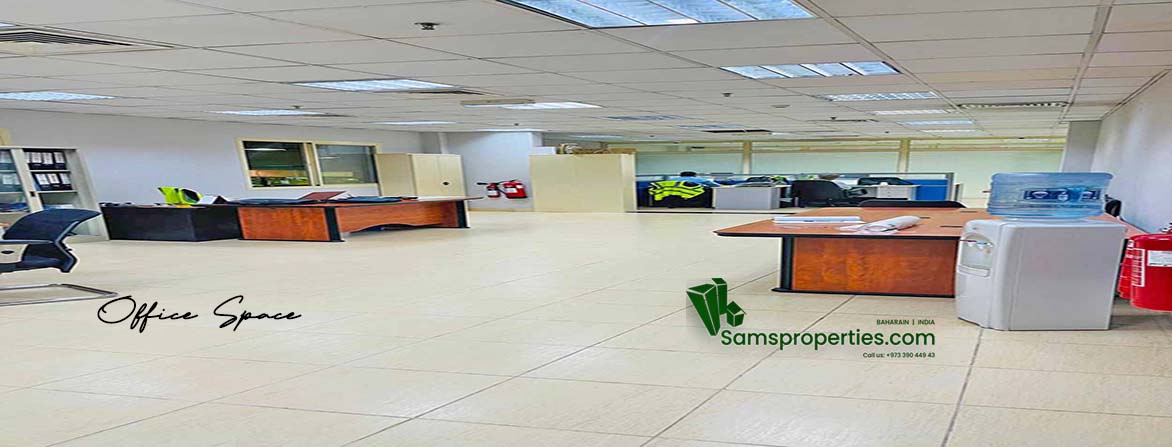 A spacious, well-lit office area within a warehouse, featuring a tiled floor, dropped ceiling with fluorescent lighting, several empty wooden desks with office chairs, filing cabinets, and a water cooler. Partitions separate different sections of the office, and a fire extinguisher is visible. The words "Office Space" are overlaid in the bottom left, and a "Samsproperties.com" logo with contact information is in the bottom right.