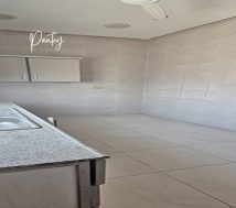 A small, empty office pantry with a sink, some cabinets, and tiled walls and floor.