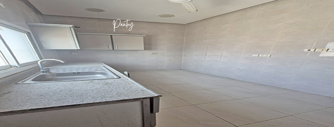 A small, empty office pantry with a sink, some cabinets, and tiled walls and floor.