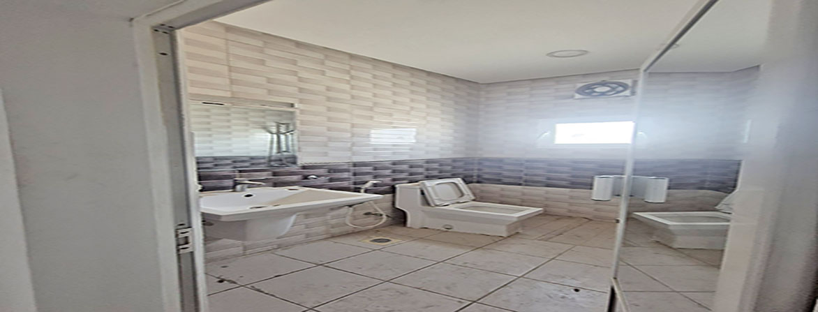 A small, empty bathroom with a white sink, a toilet, and tiled walls.