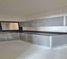Modern L-shaped kitchen with grey cabinets and black countertops in a staff flat for rent in Riffa, Bahrain.